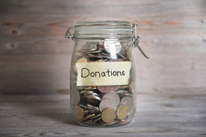 Coins in glass money jar with donations label, financial concept. Vintage wooden background with dramatic light.
